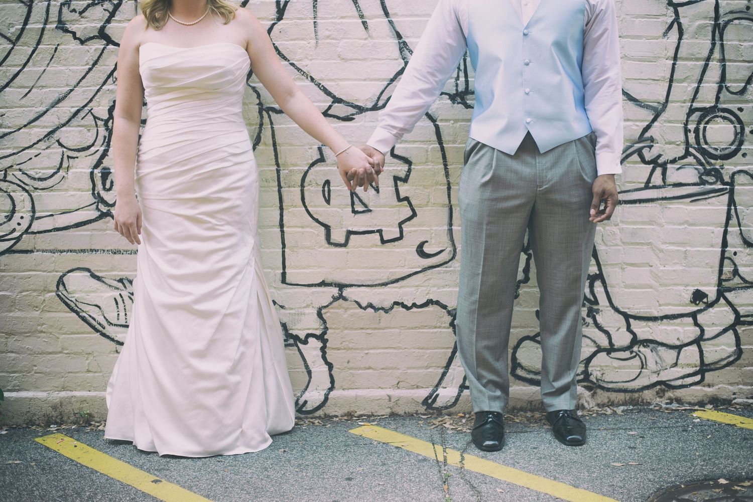 Bride and groom holding hands in front of a colorful graffiti mural wall.