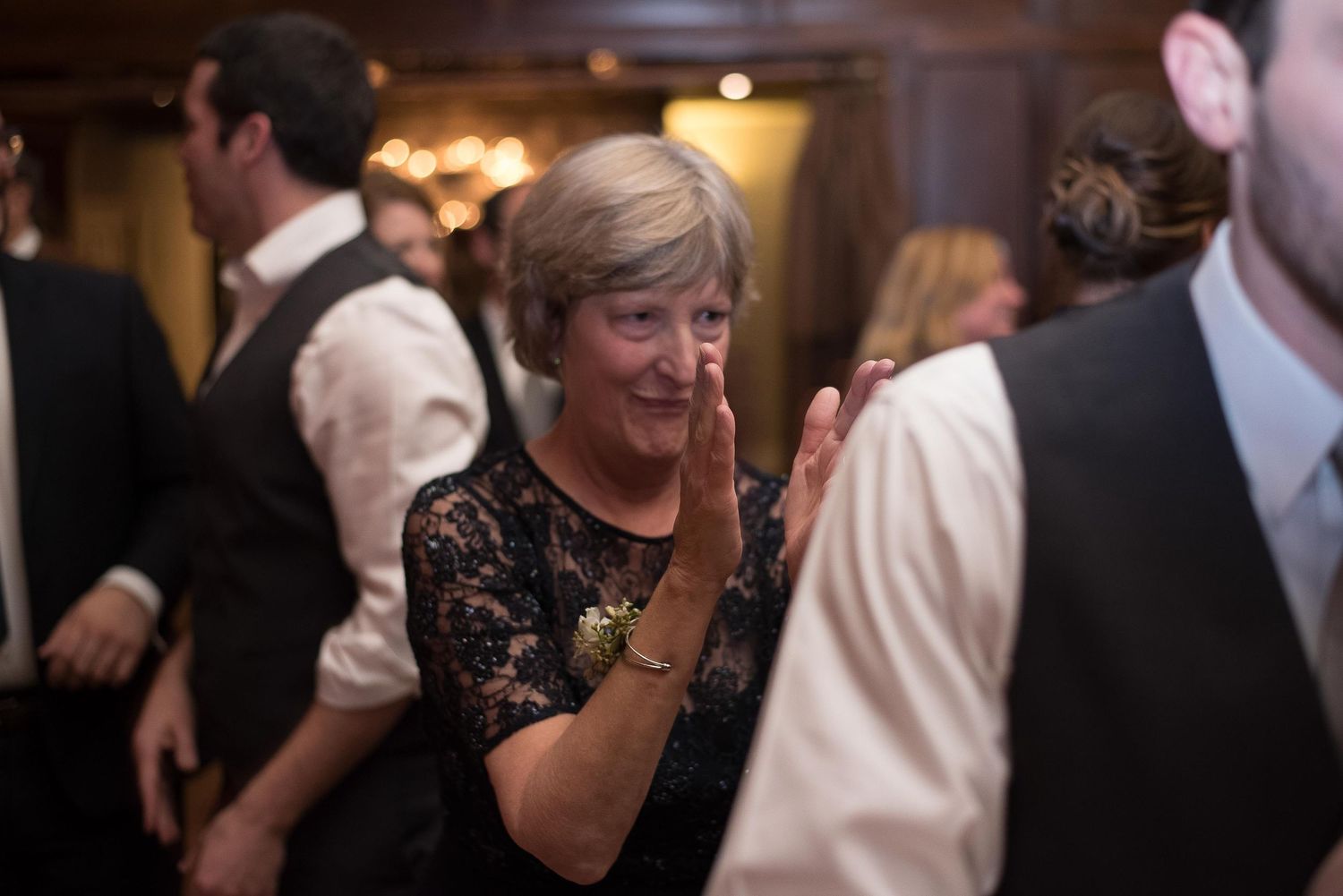 Woman in black lace dress clapping and dancing at an elegant indoor wedding reception.