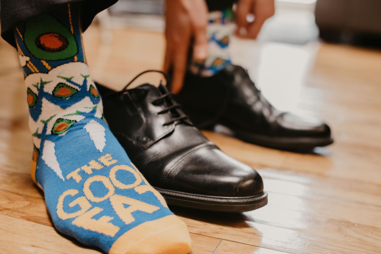 Close-up of colorful The Godfather novelty socks paired with classic black leather dress shoes on hardwood floor.