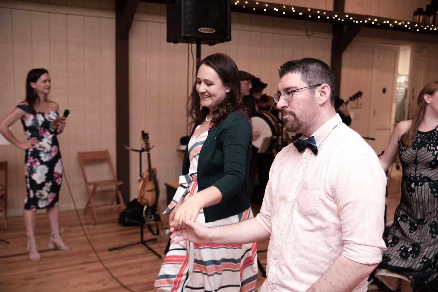 Couple dancing together at a wedding reception in a rustic barn venue with string lights and live band.