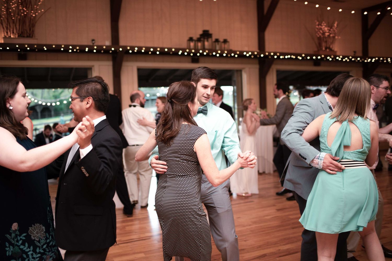 Couples dancing together at a wedding reception in a rustic barn venue with string lights.