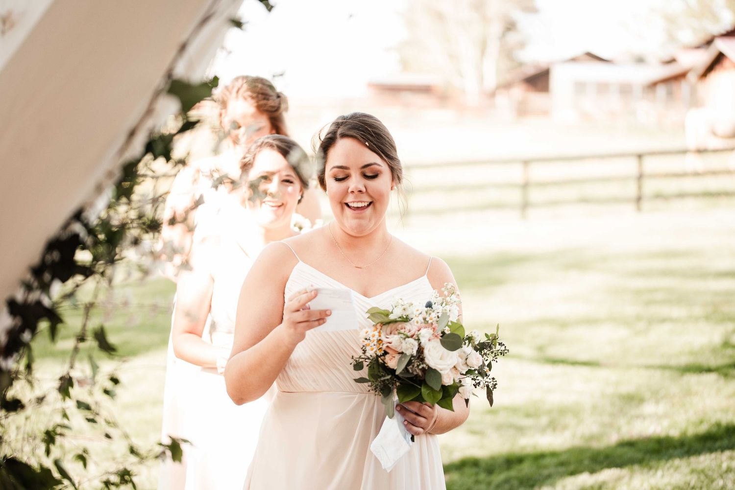 Bride in strapless gown laughing while holding pink bouquet at outdoor wedding ceremony.