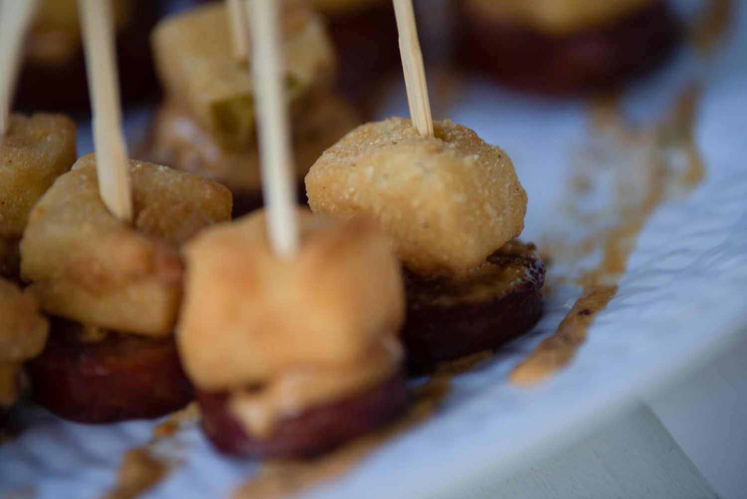 Close-up of golden fried appetizers on toothpick skewers served on a white plate.