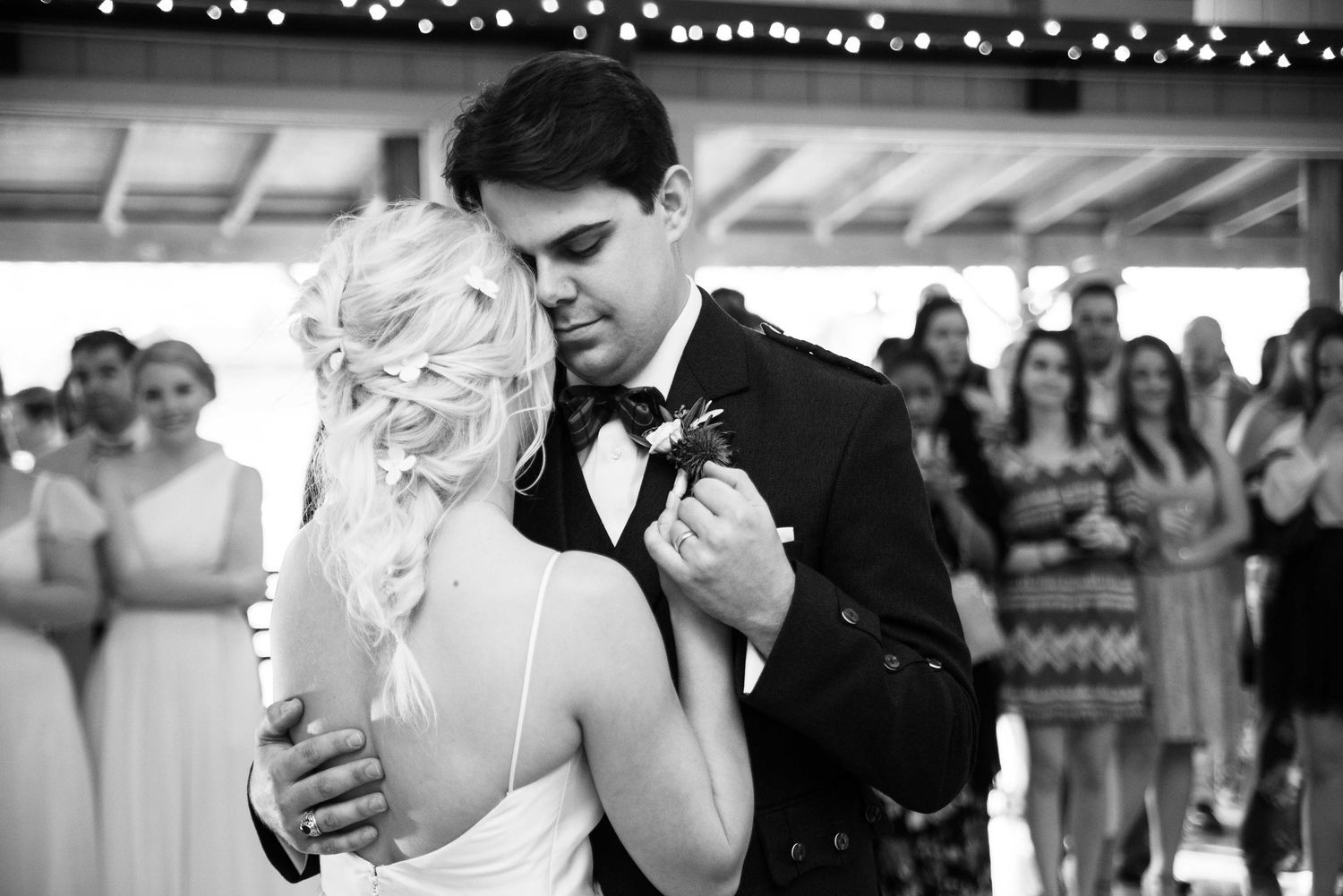 Black and white photo of bride and groom sharing their first dance at wedding reception with guests watching.