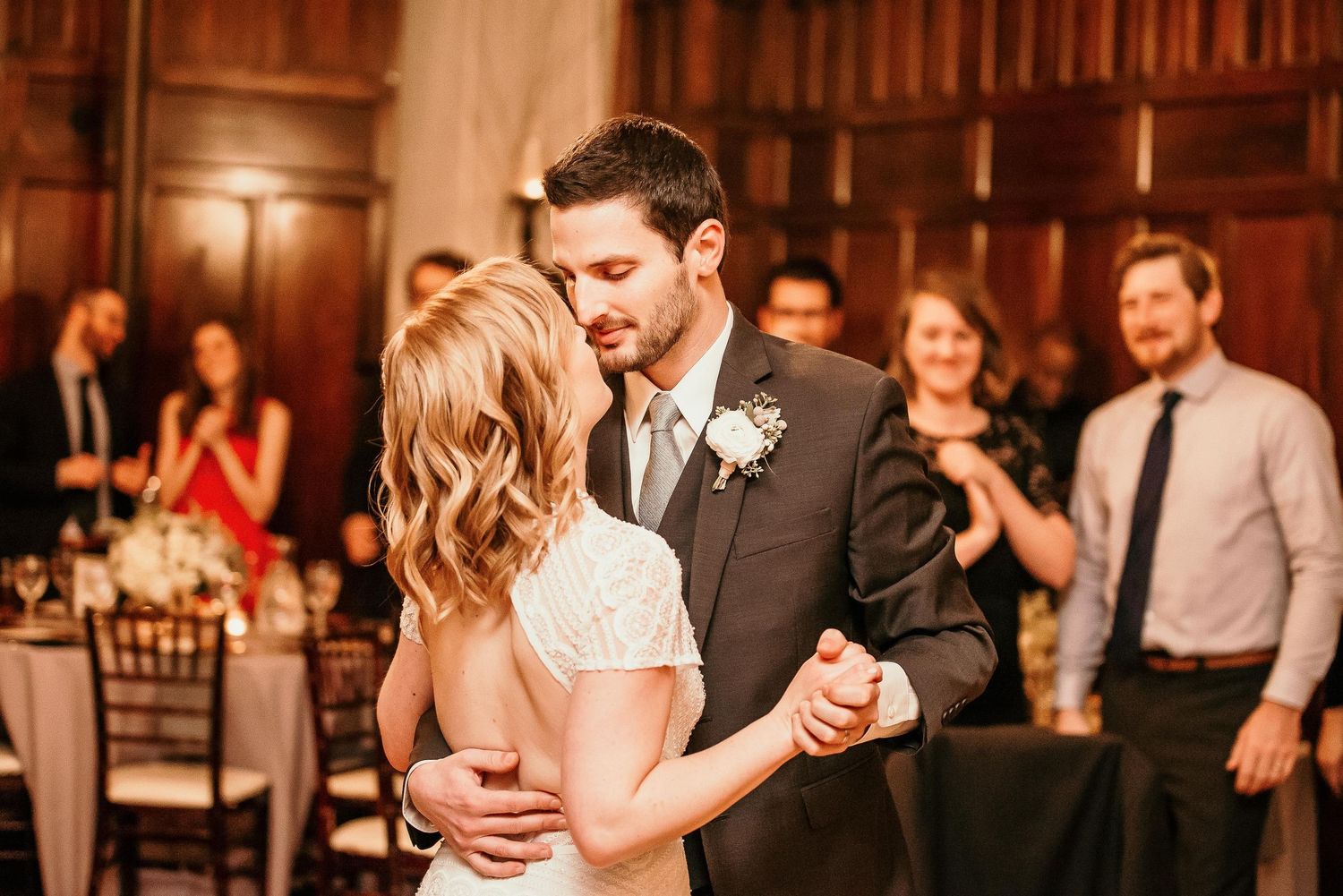 Bride and groom share their first dance at elegant wedding reception with guests watching in background.
