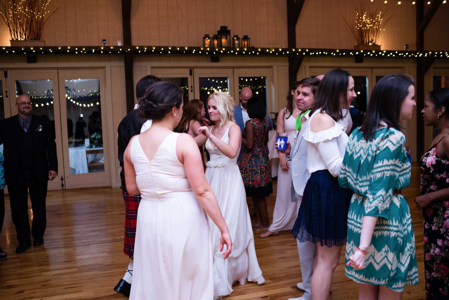 Guests dancing and celebrating at a rustic wedding reception in a warmly lit barn venue.