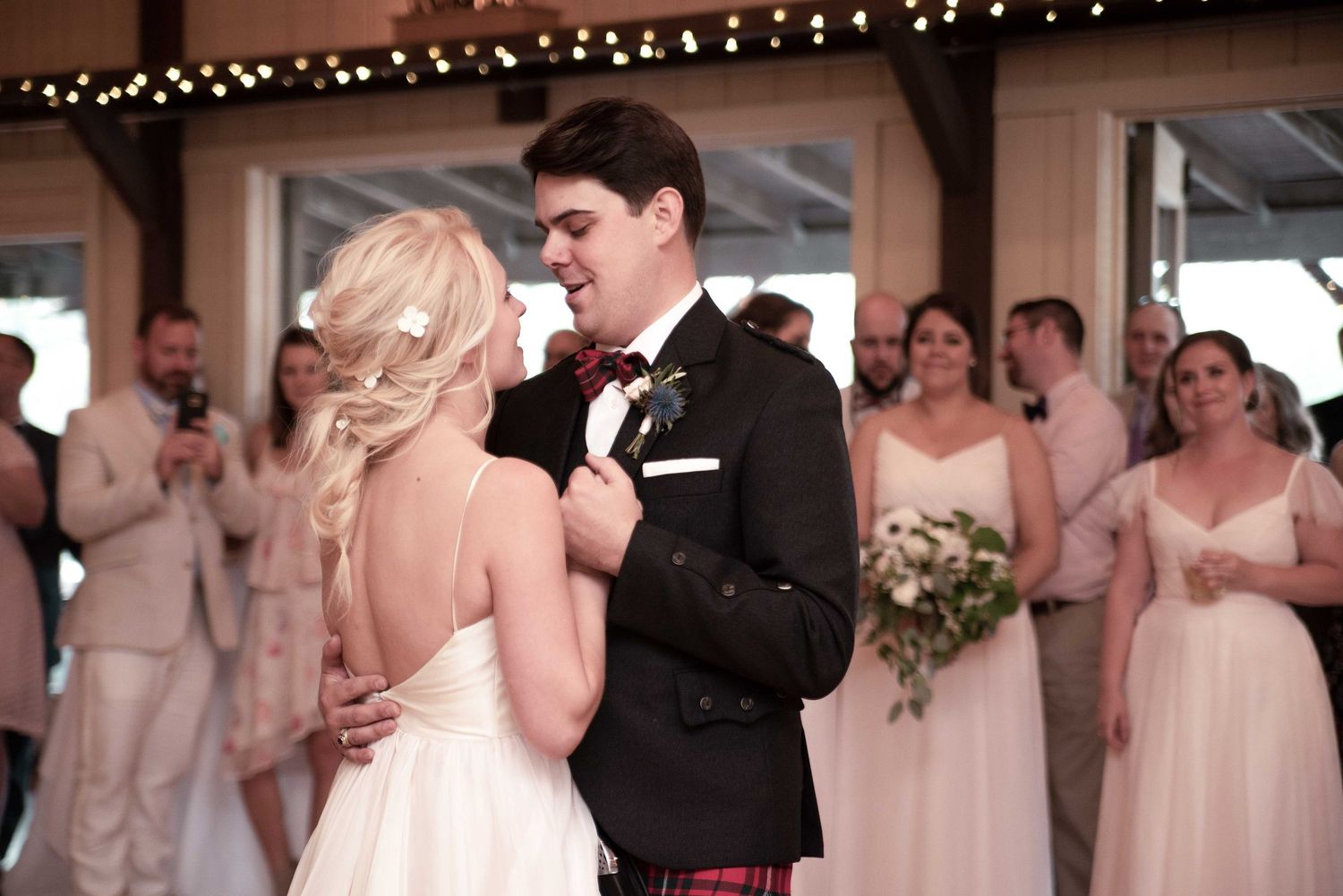 Bride and groom share first dance in rustic barn venue surrounded by wedding guests.