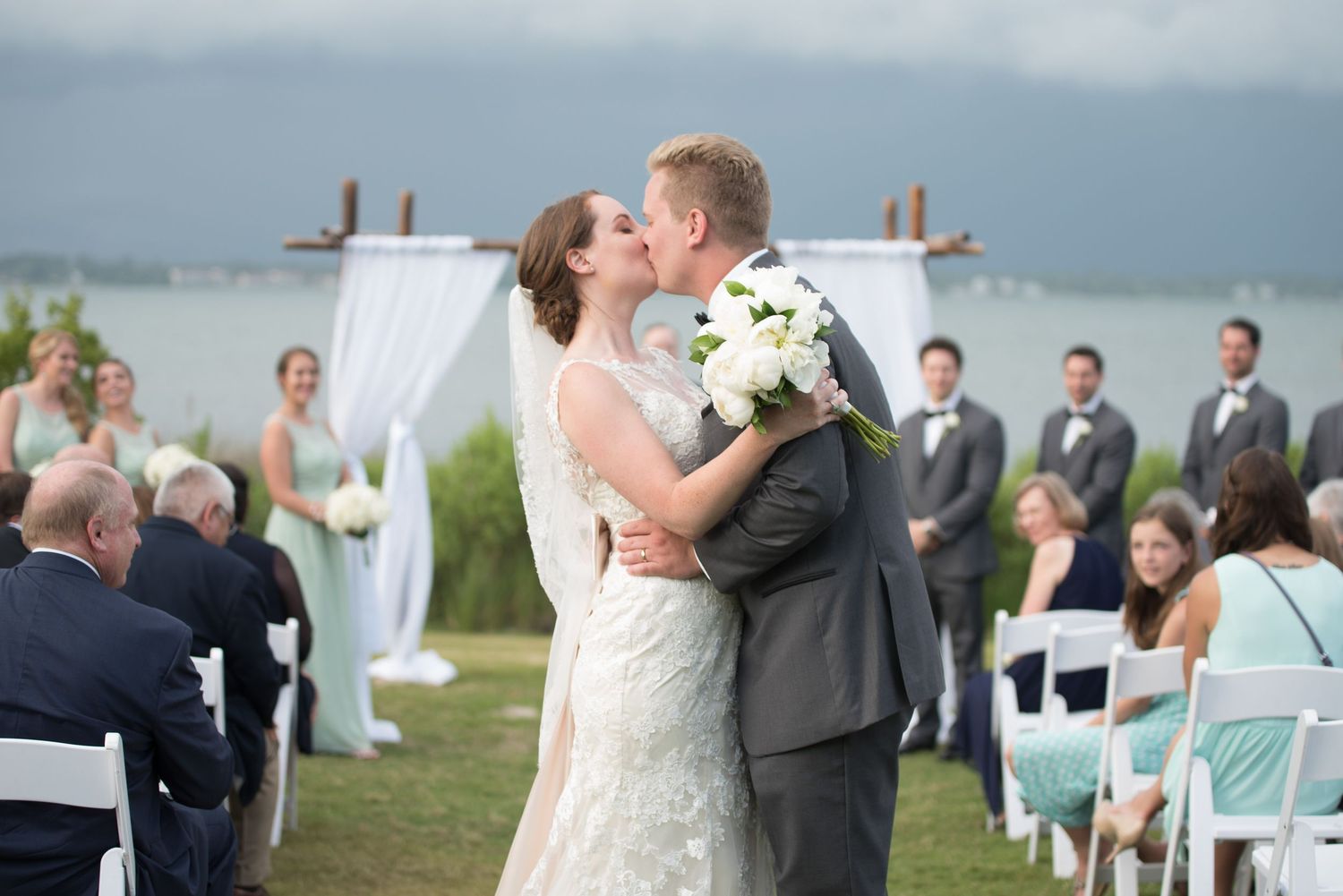 Bride and groom share first kiss at waterfront wedding ceremony.