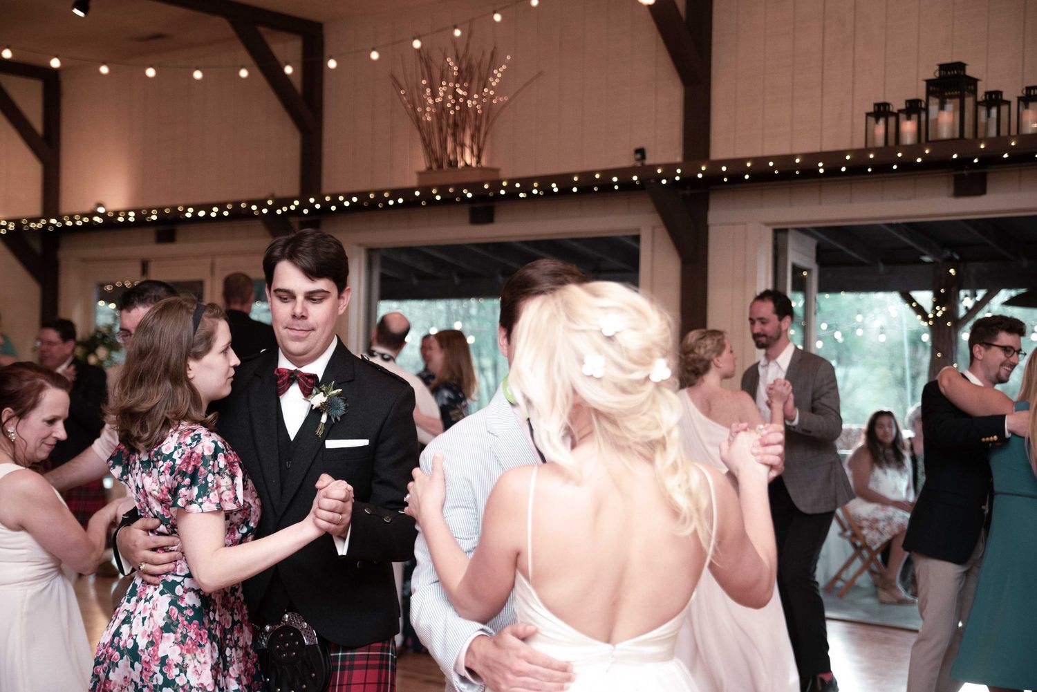 Bride and groom share a dance surrounded by guests at an elegant barn wedding reception with string lights.