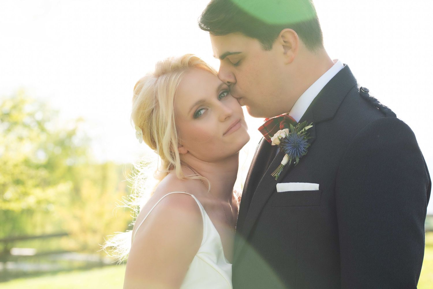A bride and groom share an intimate moment outdoors, with soft golden sunlight glowing behind them on their wedding day.