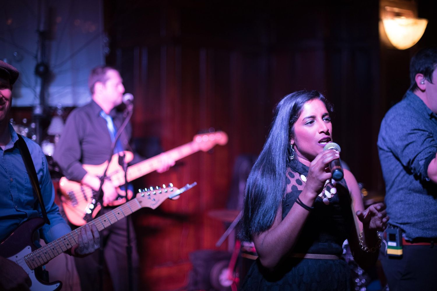 Live band performance with female vocalist singing into microphone and guitarist playing electric guitar on stage.