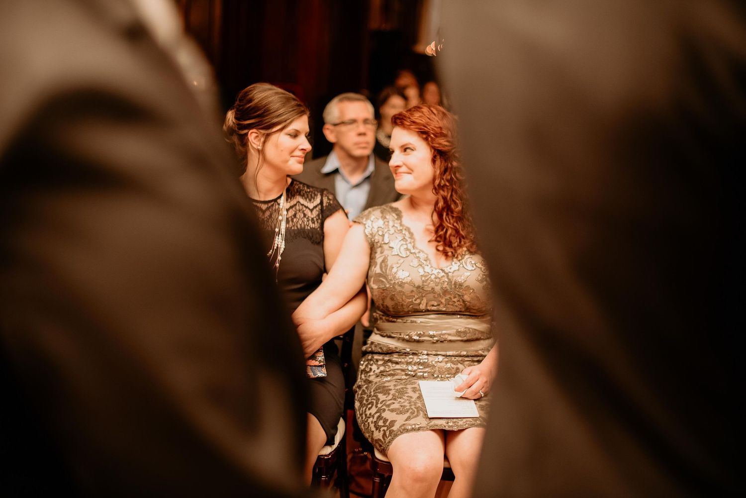 Two women in elegant dresses smiling and chatting at a formal event or wedding reception.