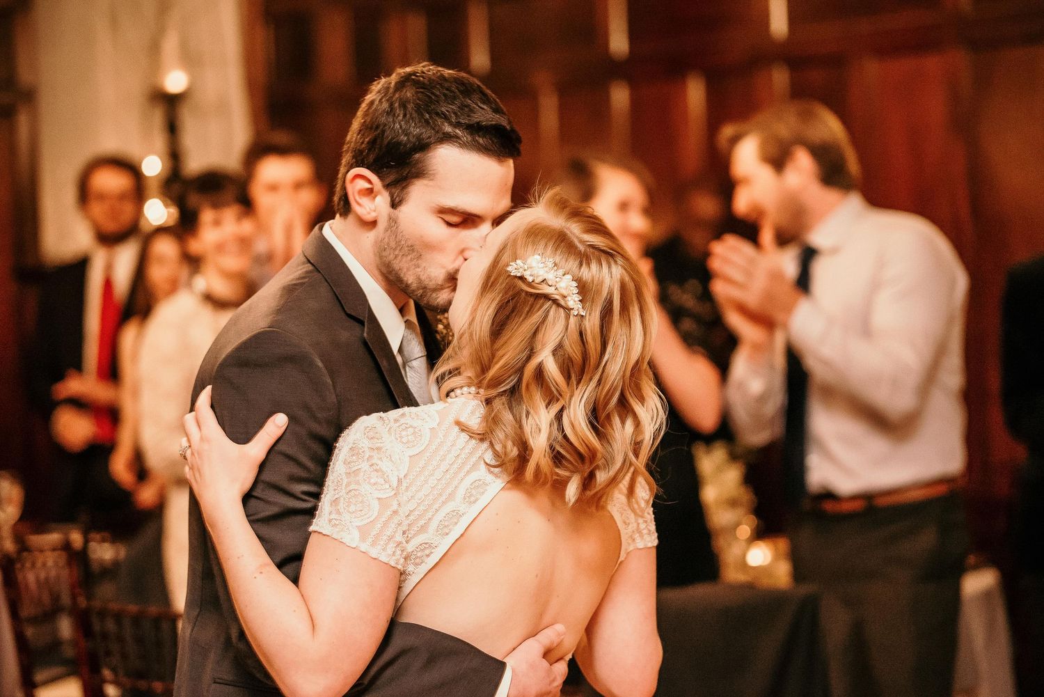 Bride and groom share their first dance kiss at a romantic wedding reception with guests applauding in the background.