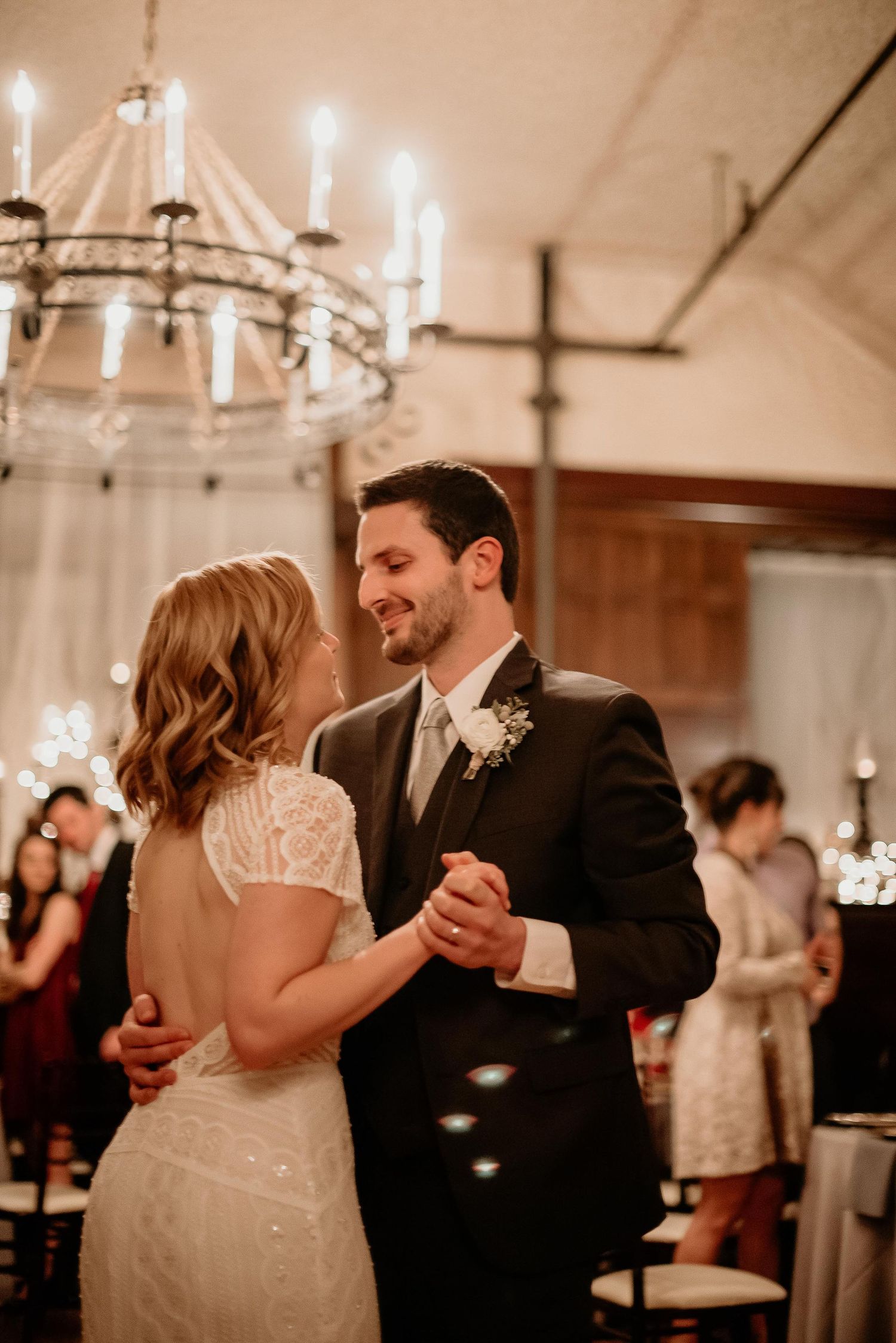 A bride and groom share their first dance beneath a candlelit chandelier at an elegant wedding reception.