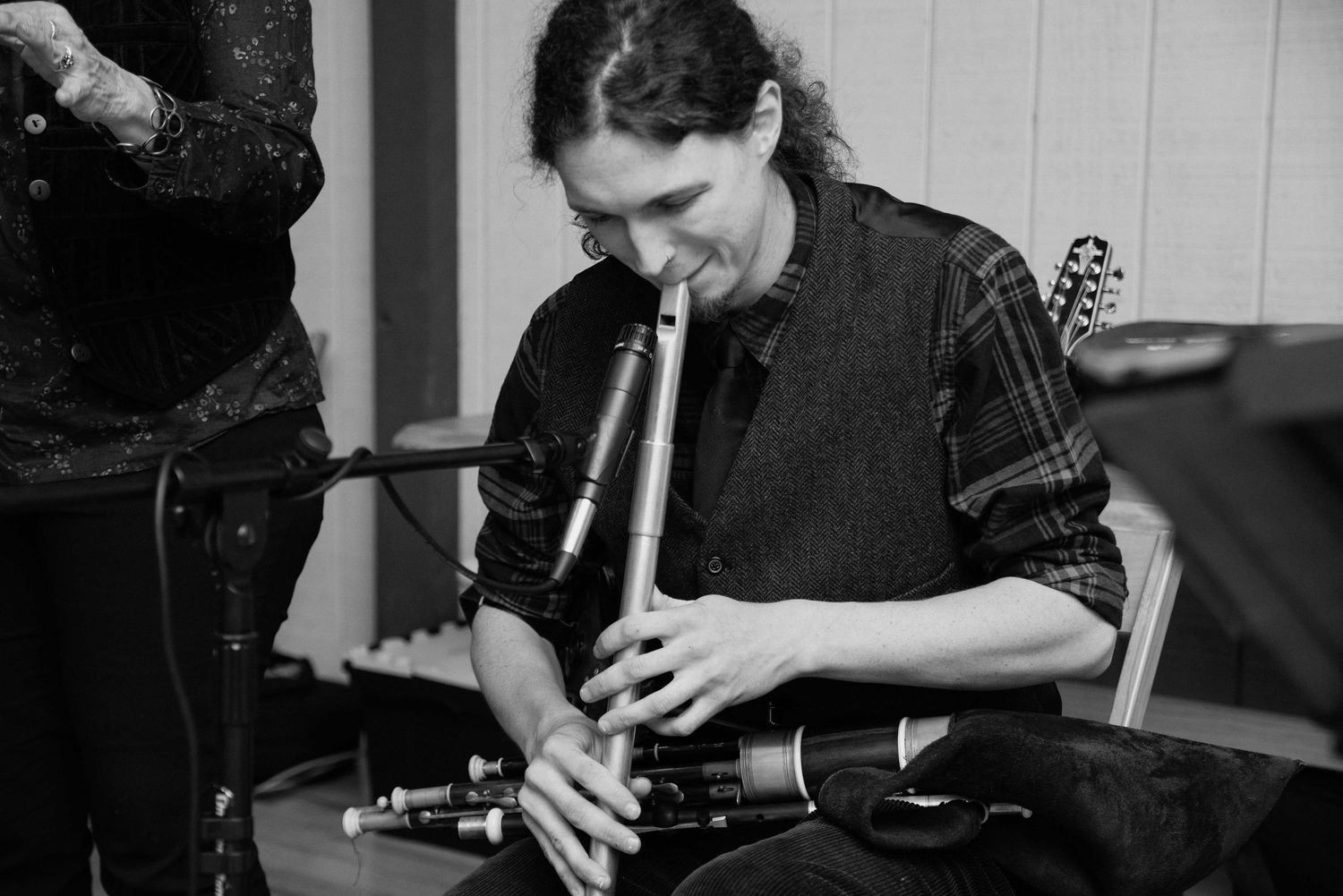Musician playing uilleann pipes in black and white photo, focused expression, indoor setting.