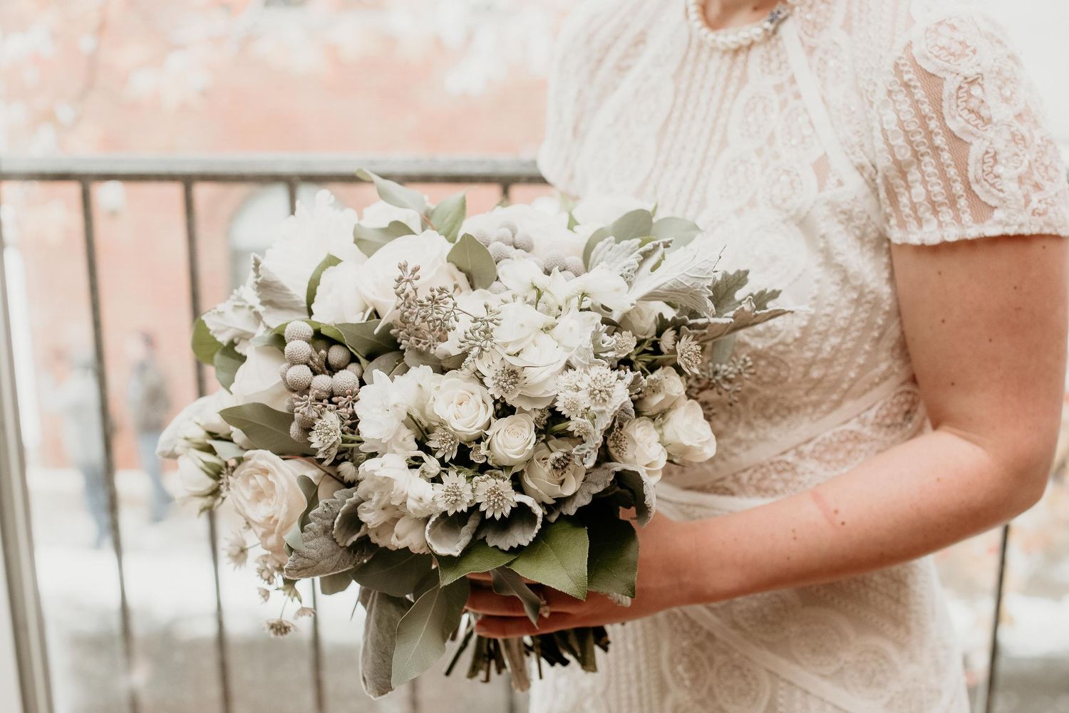 Bride holding a lush white and sage green wedding bouquet with roses and eucalyptus, wearing a lace gown.