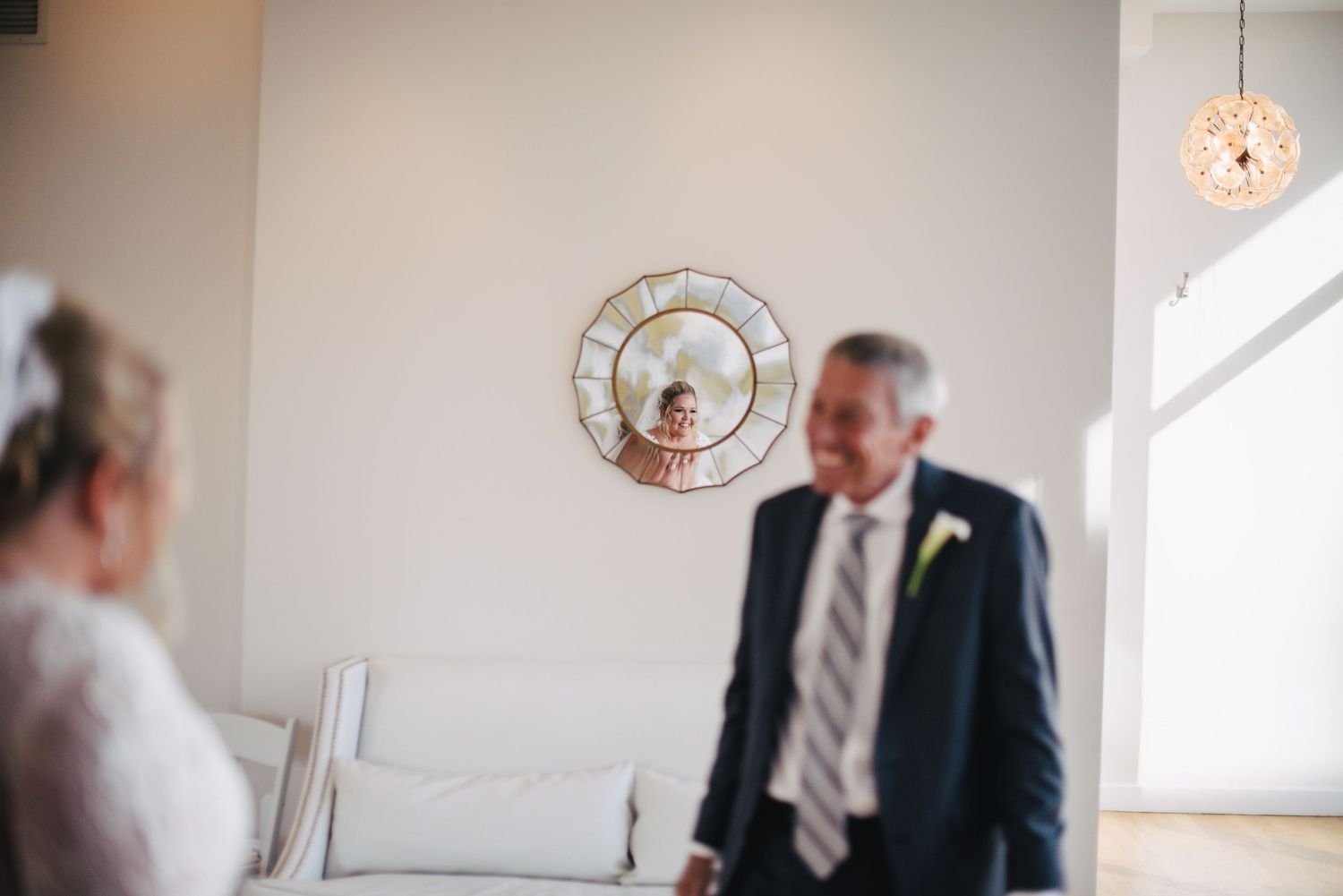 Bride's reflection appears in a decorative mirror as she shares a first look moment with her father.