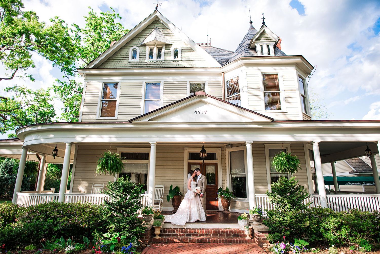 Bride and groom pose on steps of a charming Victorian white house with wrap-around porch.