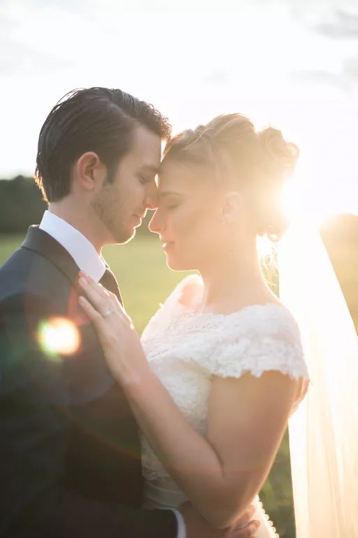 Bride and groom share a romantic moment with golden sunset backlight in a field.
