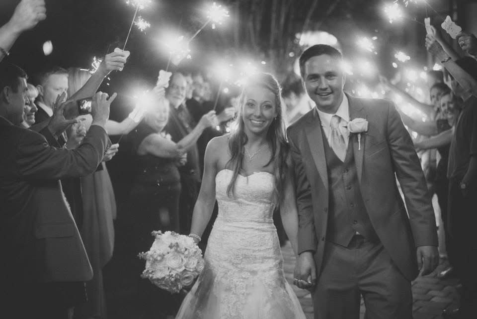 Black and white wedding photo of bride and groom walking through a sparkler send-off celebration.