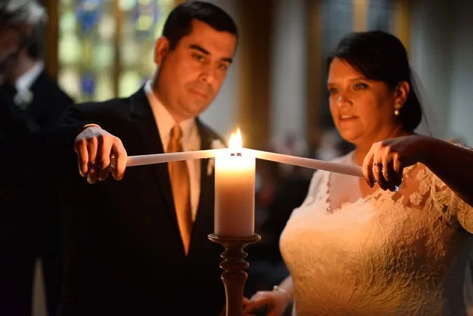 Bride and groom perform a unity candle ceremony together during their romantic church wedding.