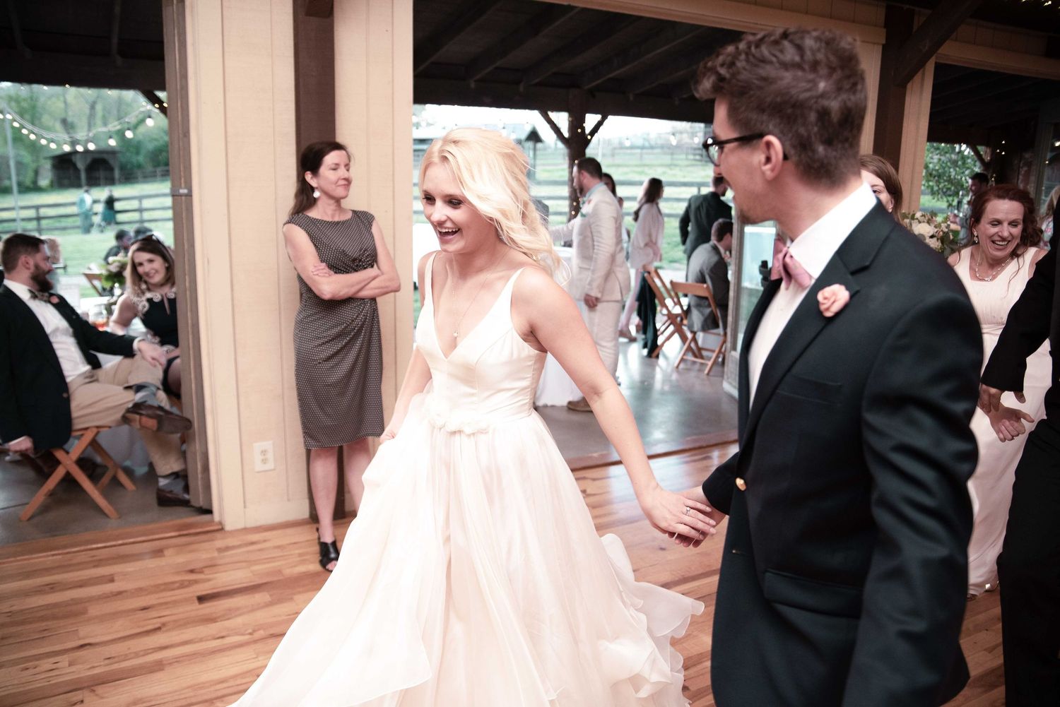 Bride in white gown and groom in dark suit share a joyful first dance at rustic outdoor wedding reception.