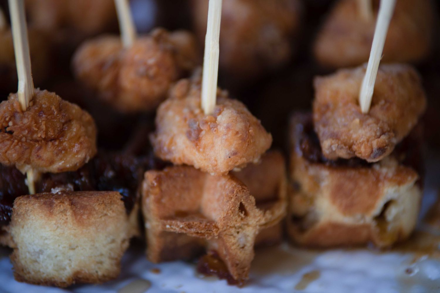 Crispy fried food bites skewered on toothpicks, served as appetizers or tapas on white paper.