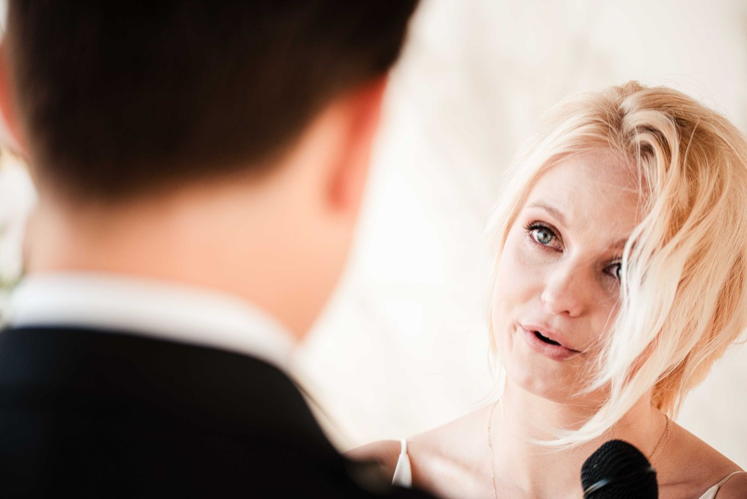 Emotional blonde bride gazing at groom during wedding ceremony, captured in an intimate close-up portrait.
