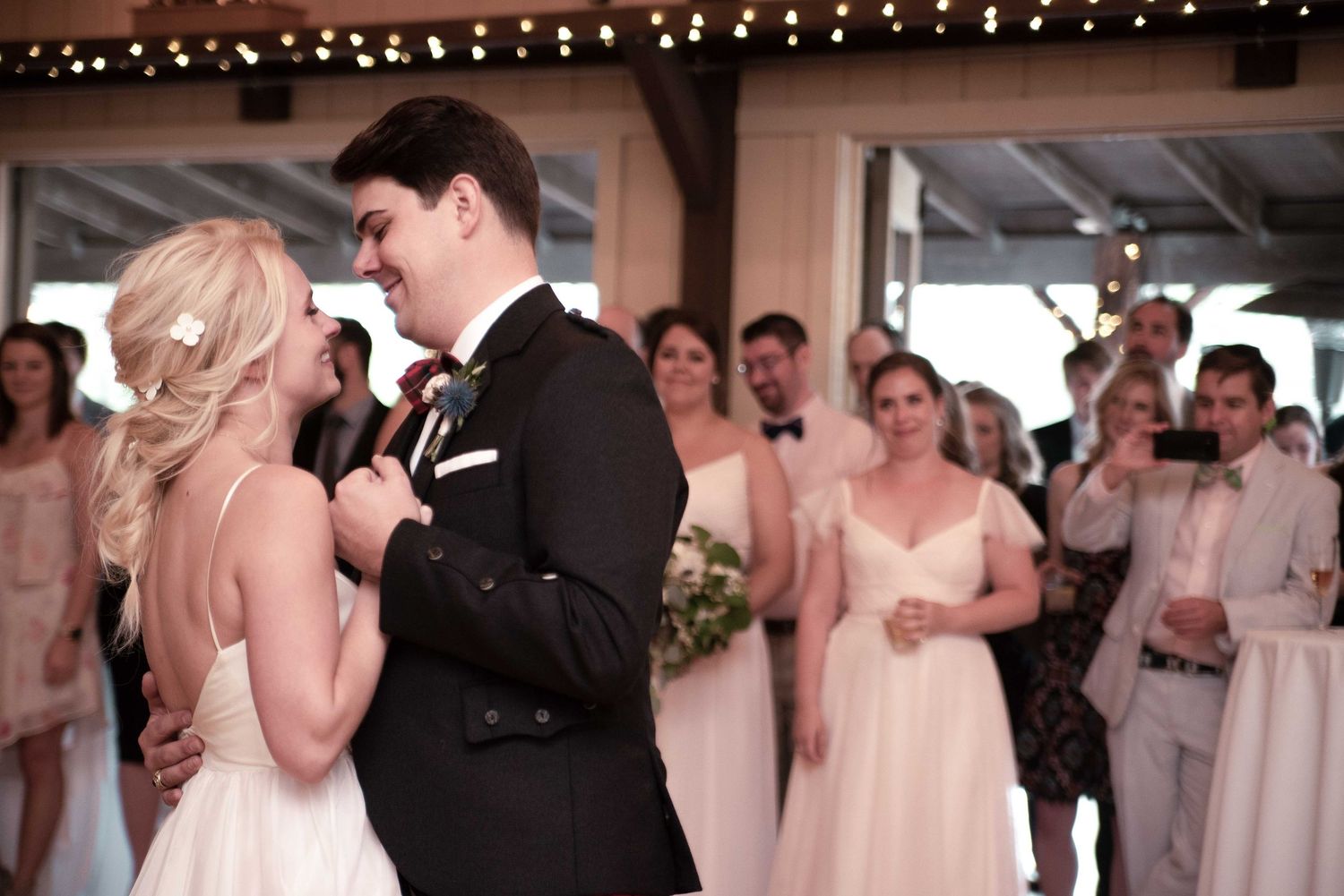 Bride and groom share their first dance at a wedding reception with bridesmaids in pink gowns watching in background.