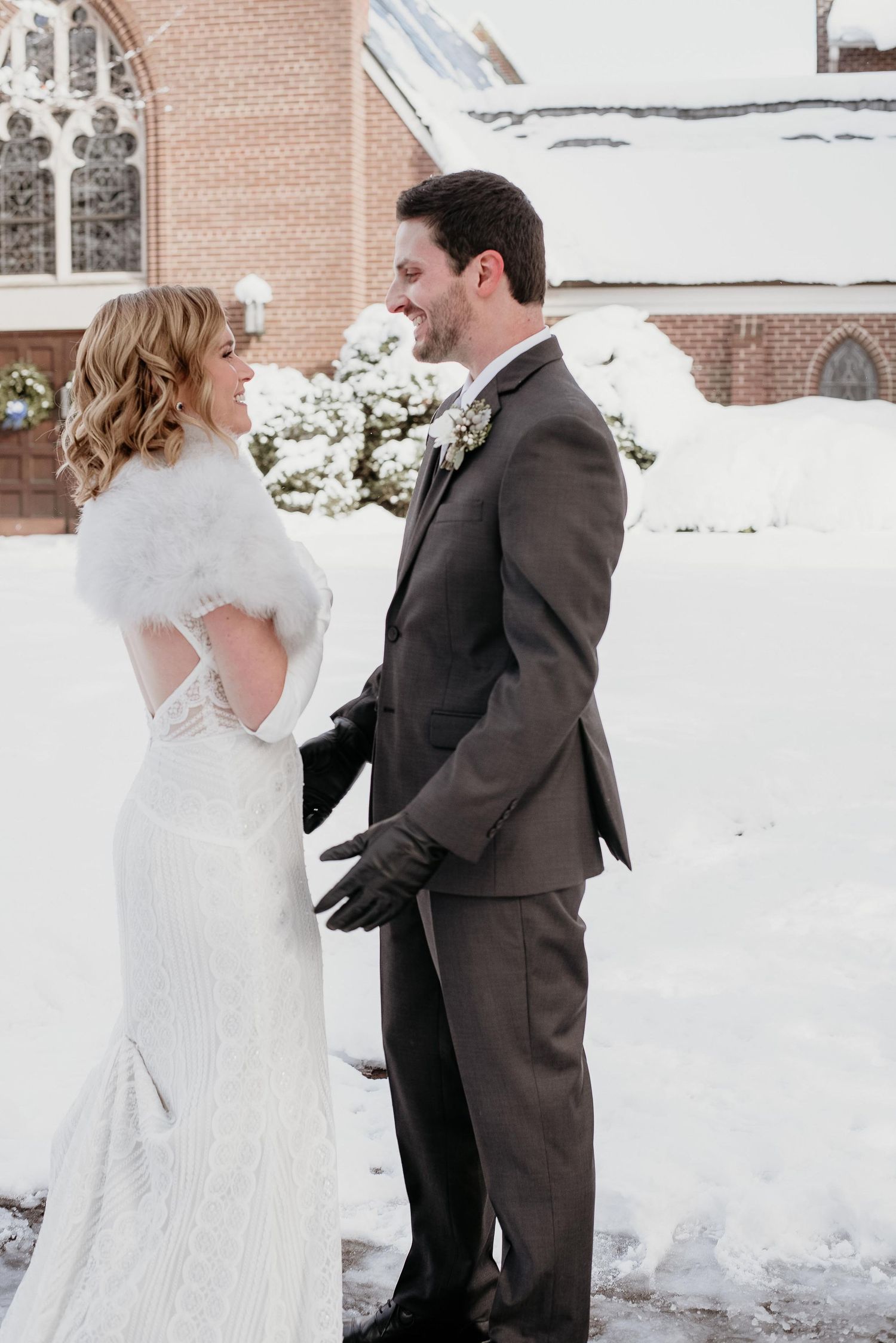 Bride and groom share a romantic moment outside a snow-covered church in winter wedding attire.