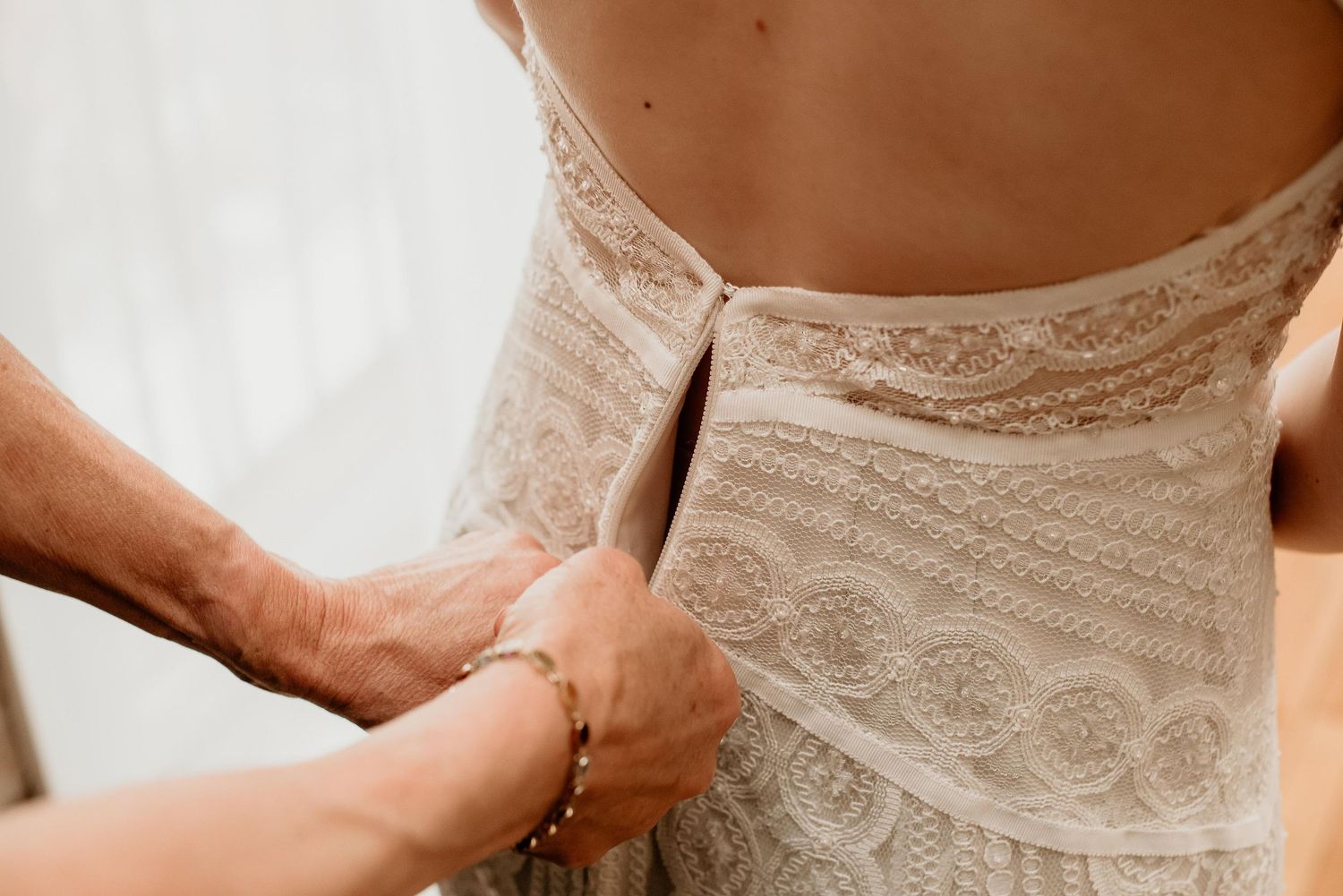 Close-up of hands fastening the back of a lace wedding dress on a bride.