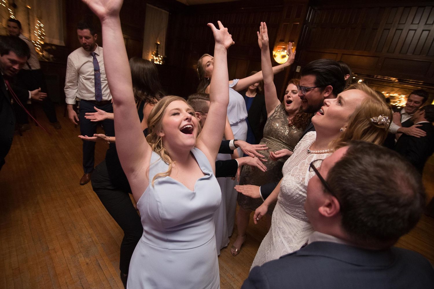Excited wedding guests dancing with arms raised at a lively indoor wedding reception.