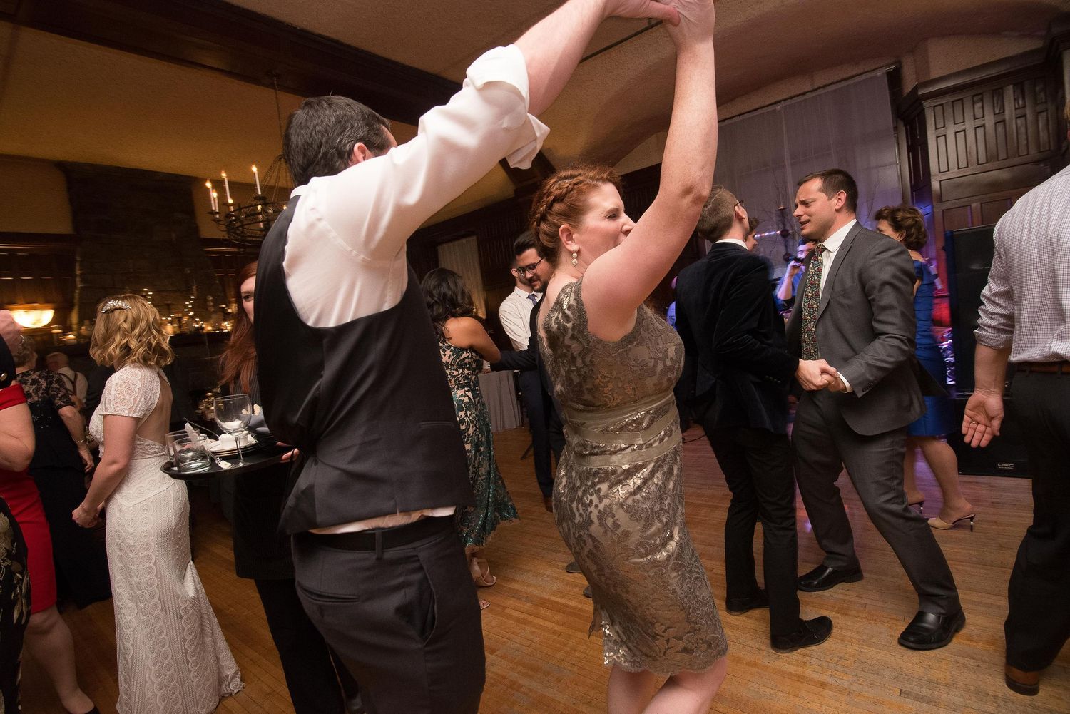 Couples dancing energetically at a wedding reception in an elegant venue with warm lighting.