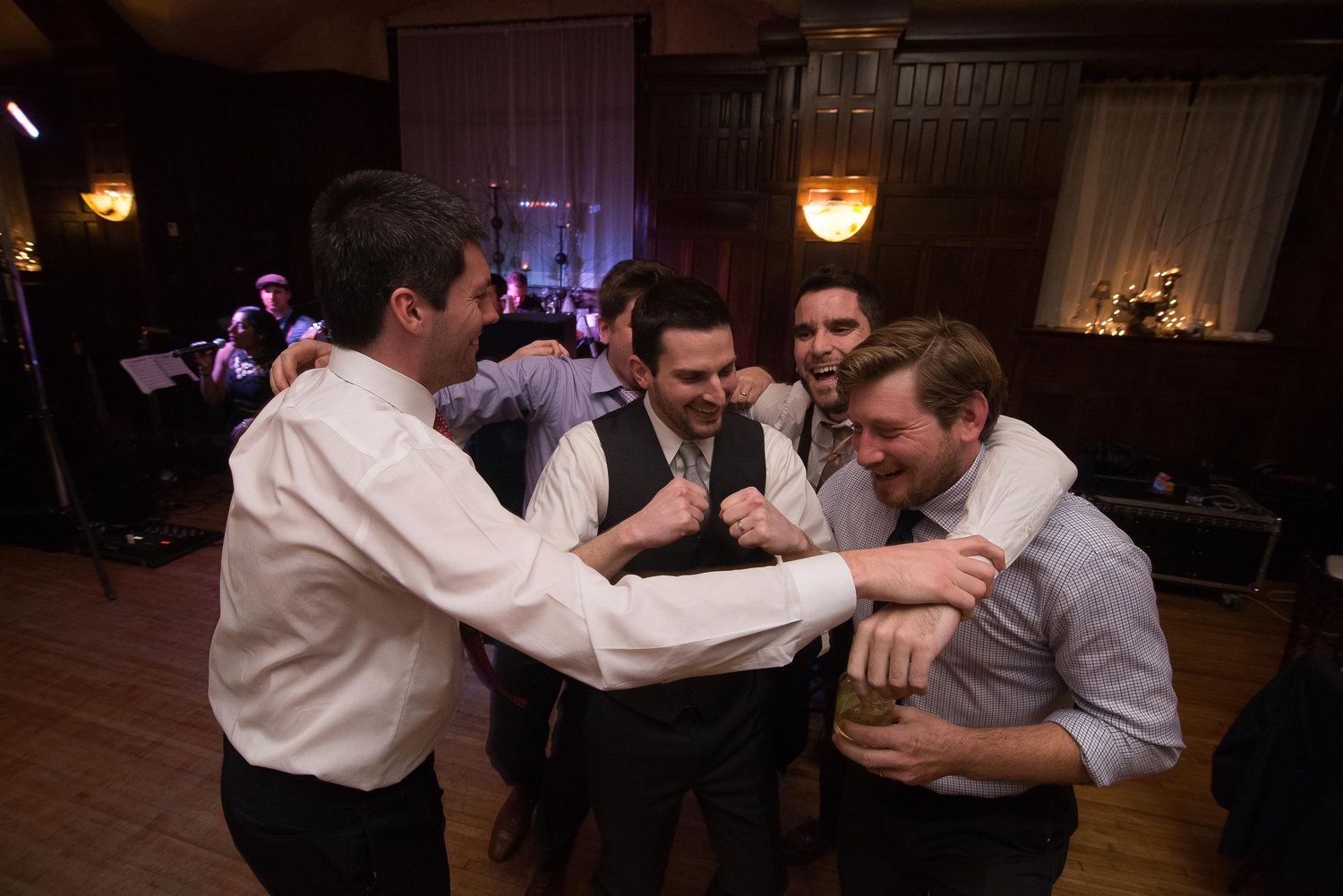 Group of men in dress shirts celebrating on a wedding reception dance floor in a dimly lit venue.