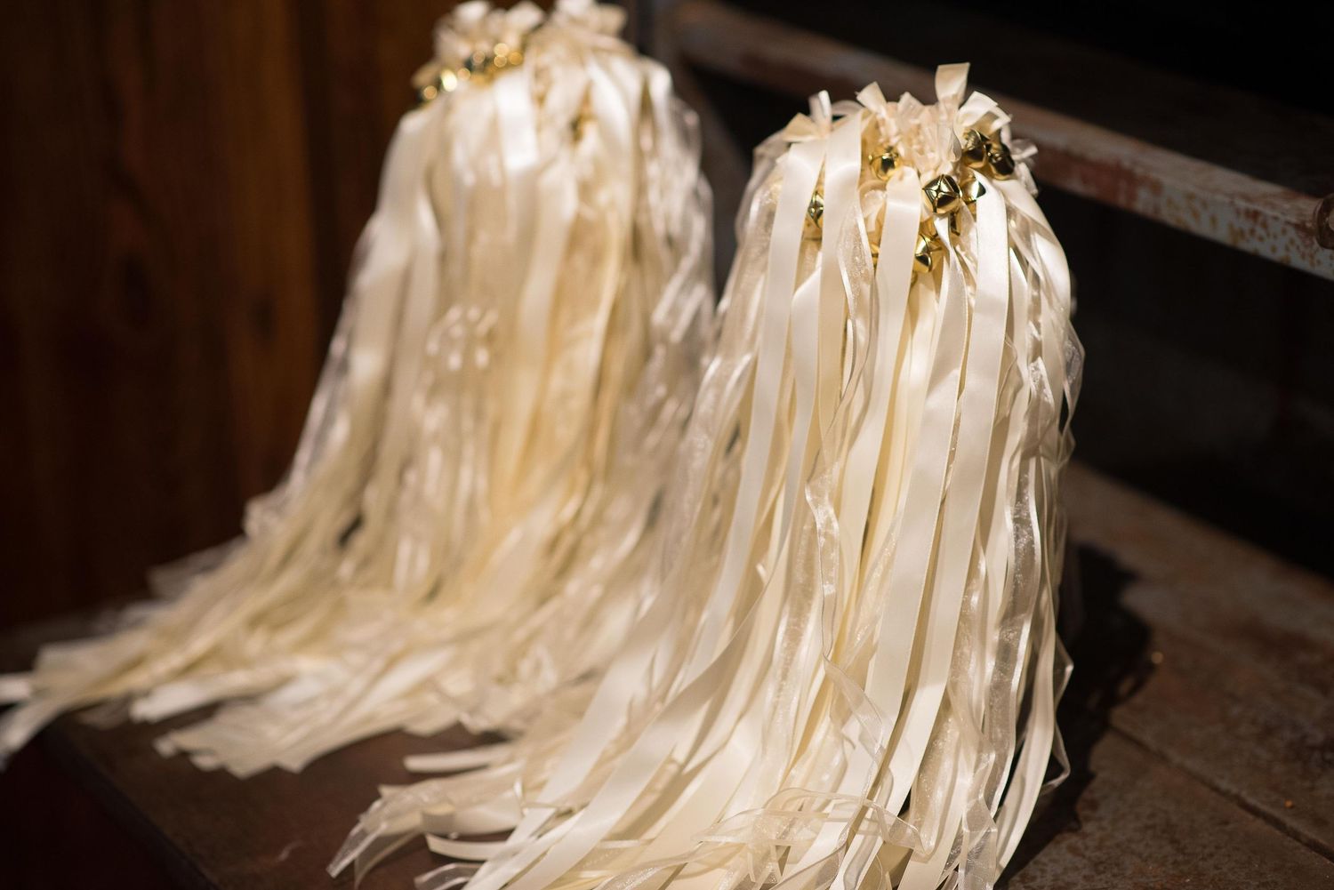 Elegant ivory ribbon wands with gold bell accents displayed on a wooden surface for a wedding ceremony.