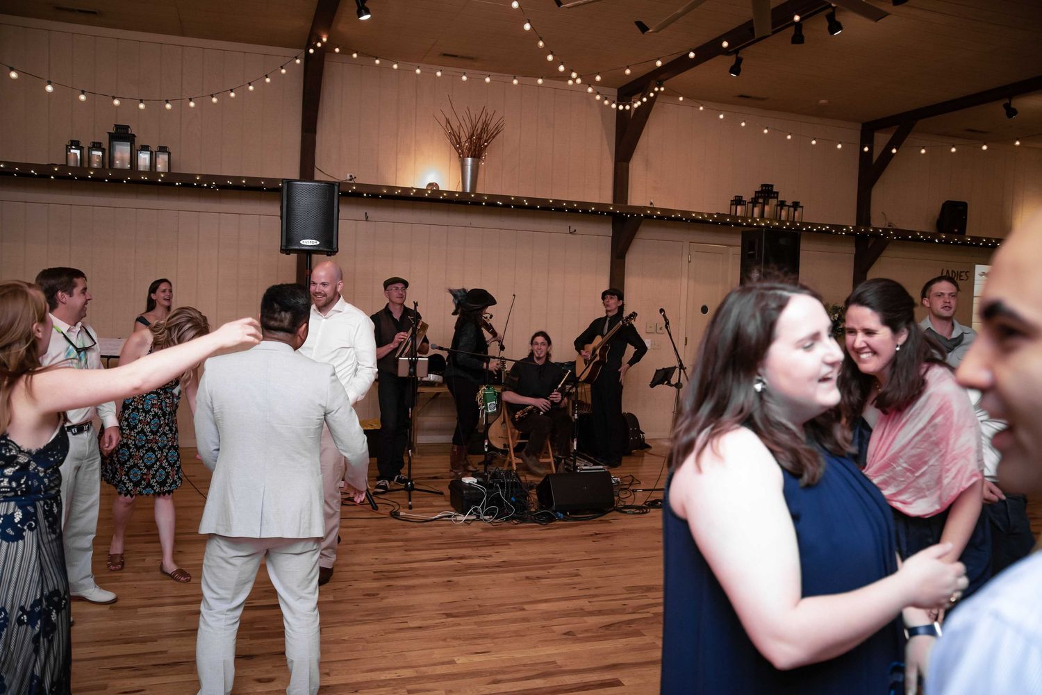 Guests dancing at a wedding reception with a live string band performing in a decorated venue with string lights.