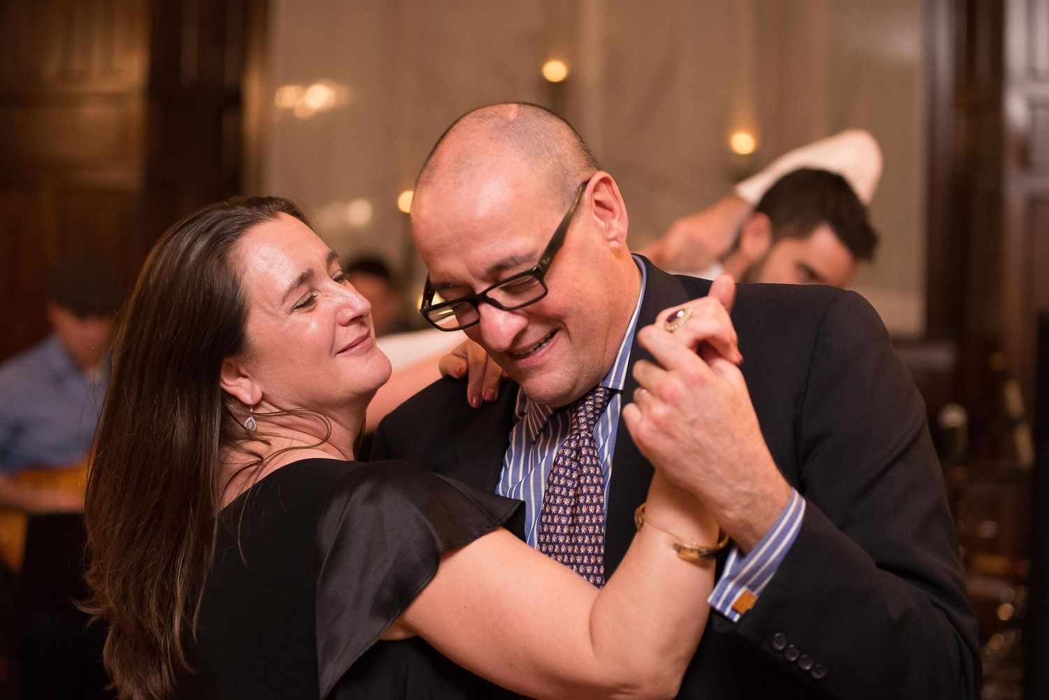 Couple sharing a joyful dance embrace at an elegant indoor event, smiling warmly at each other.