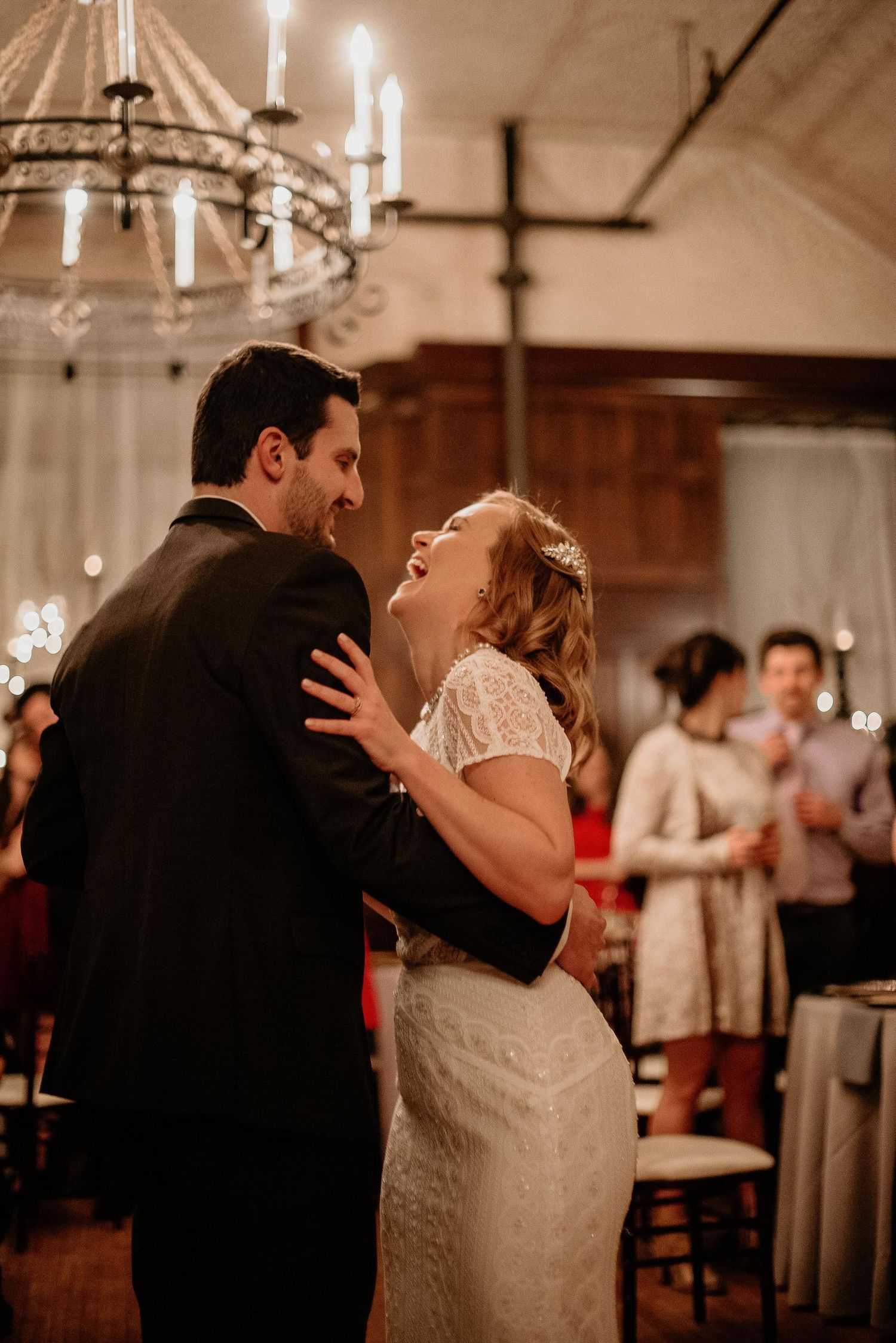 Bride laughing joyfully during first dance with groom at elegant candlelit wedding reception.