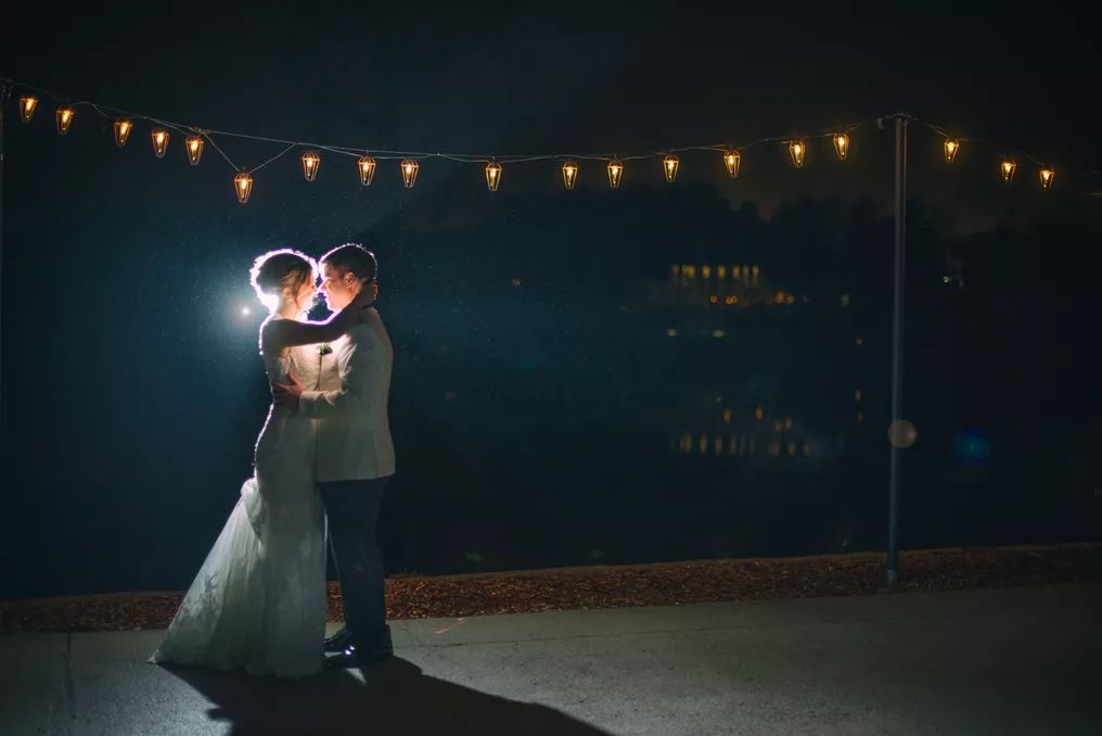 Bride and groom sharing a romantic kiss under string lights at night wedding reception.