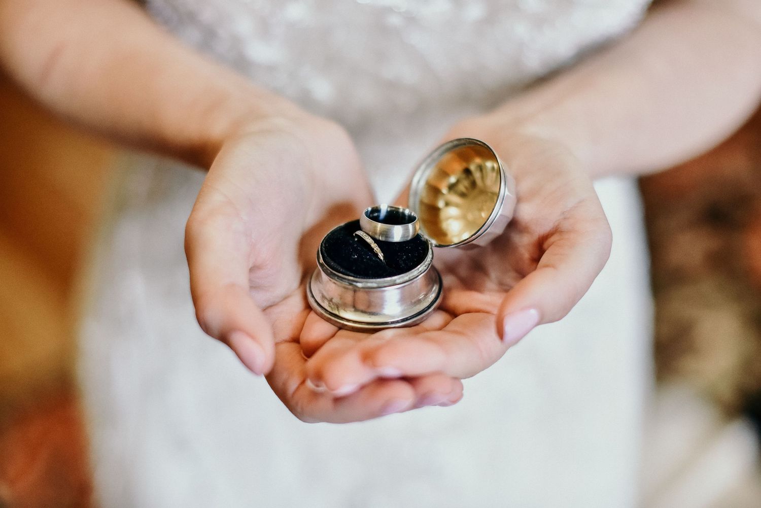 Bride holds open a vintage ring box displaying wedding bands in her delicate hands.