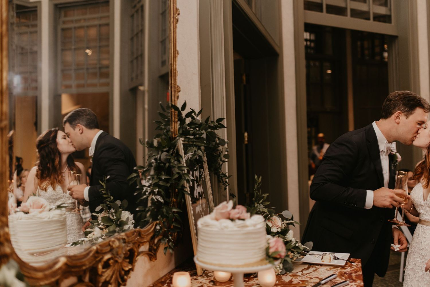 Bride and groom sharing a kiss beside a white wedding cake at indoor reception.
