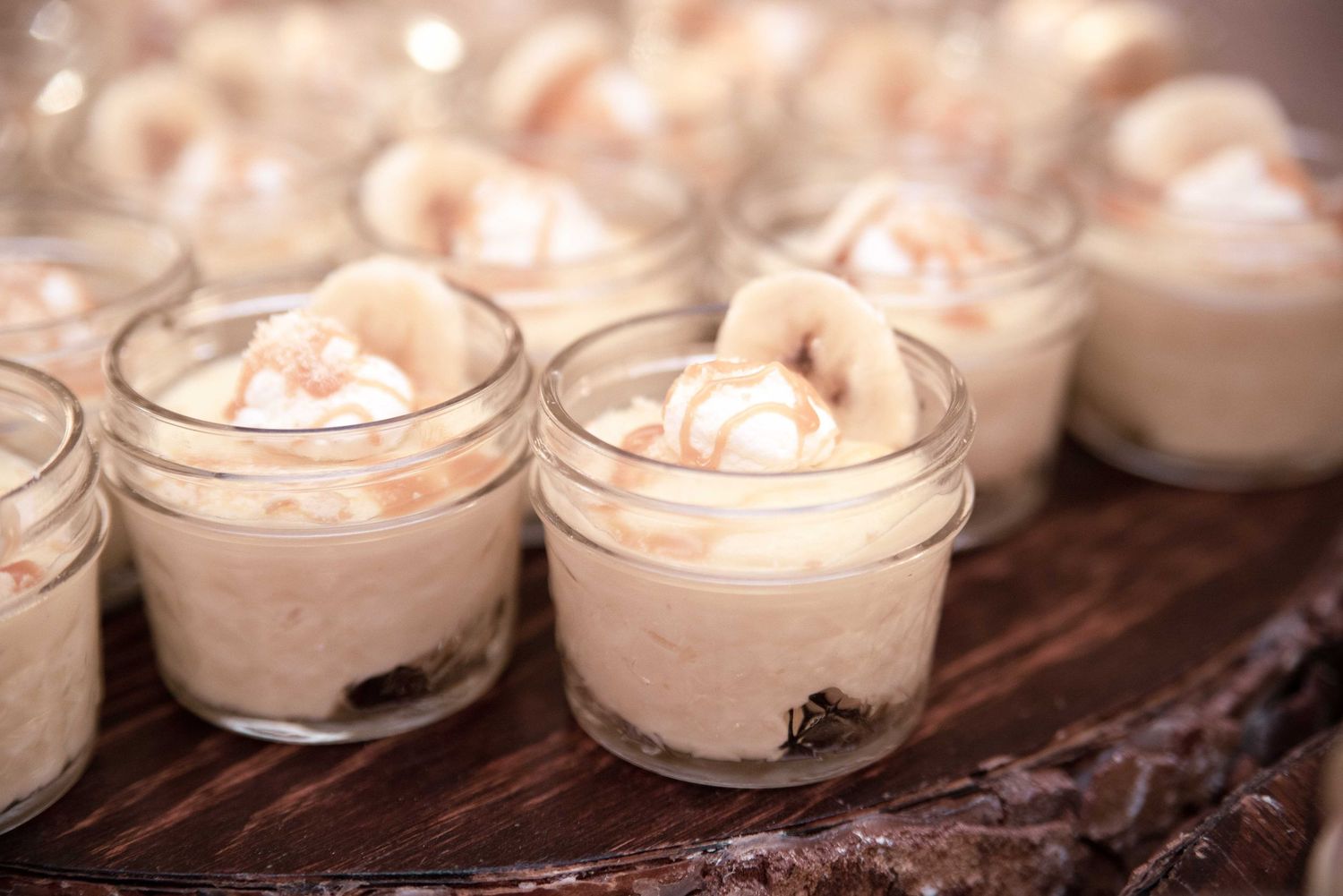 Mason jars filled with creamy banana pudding dessert topped with whipped cream and banana slices at a wedding reception.