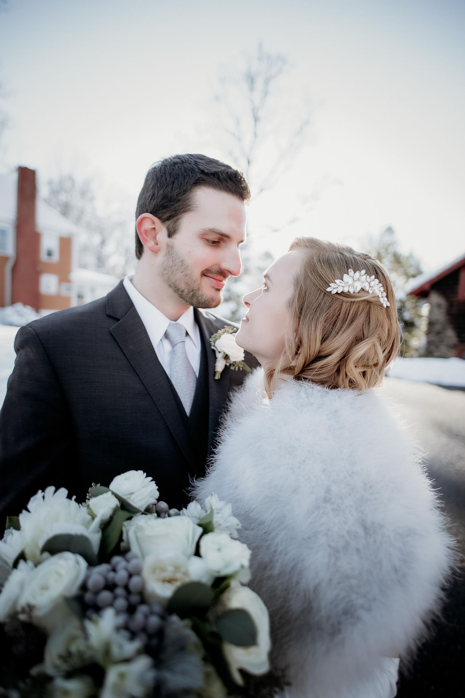 Bride and groom share a romantic winter moment, she holds white floral bouquet wearing fur wrap and crystal headpiece.