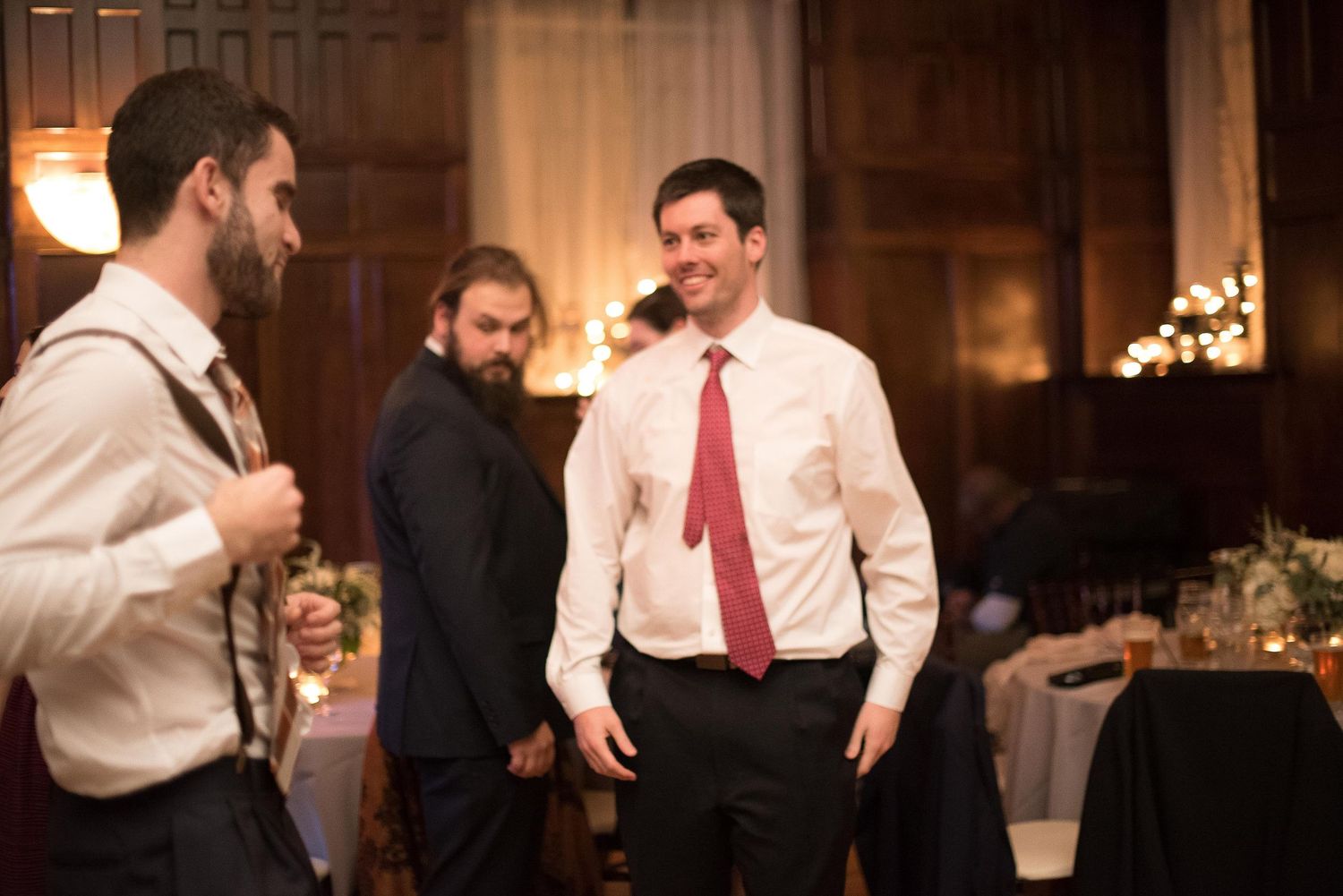 Men in formal attire socializing at an elegant wedding reception venue with warm ambient lighting.