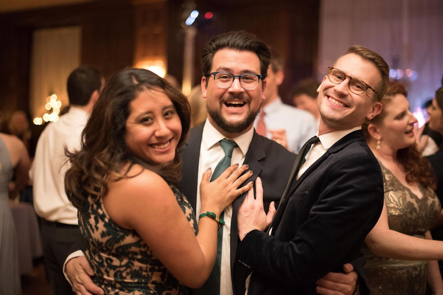 Three friends smiling and laughing together at a formal wedding reception party event.