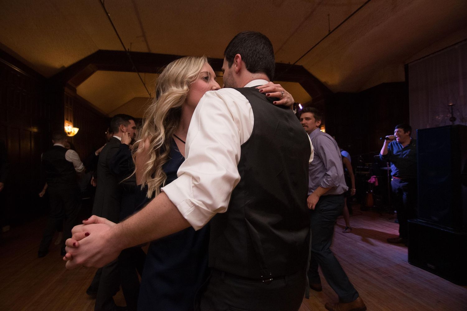 Couple sharing a romantic kiss while slow dancing at a wedding reception in a warmly lit venue.