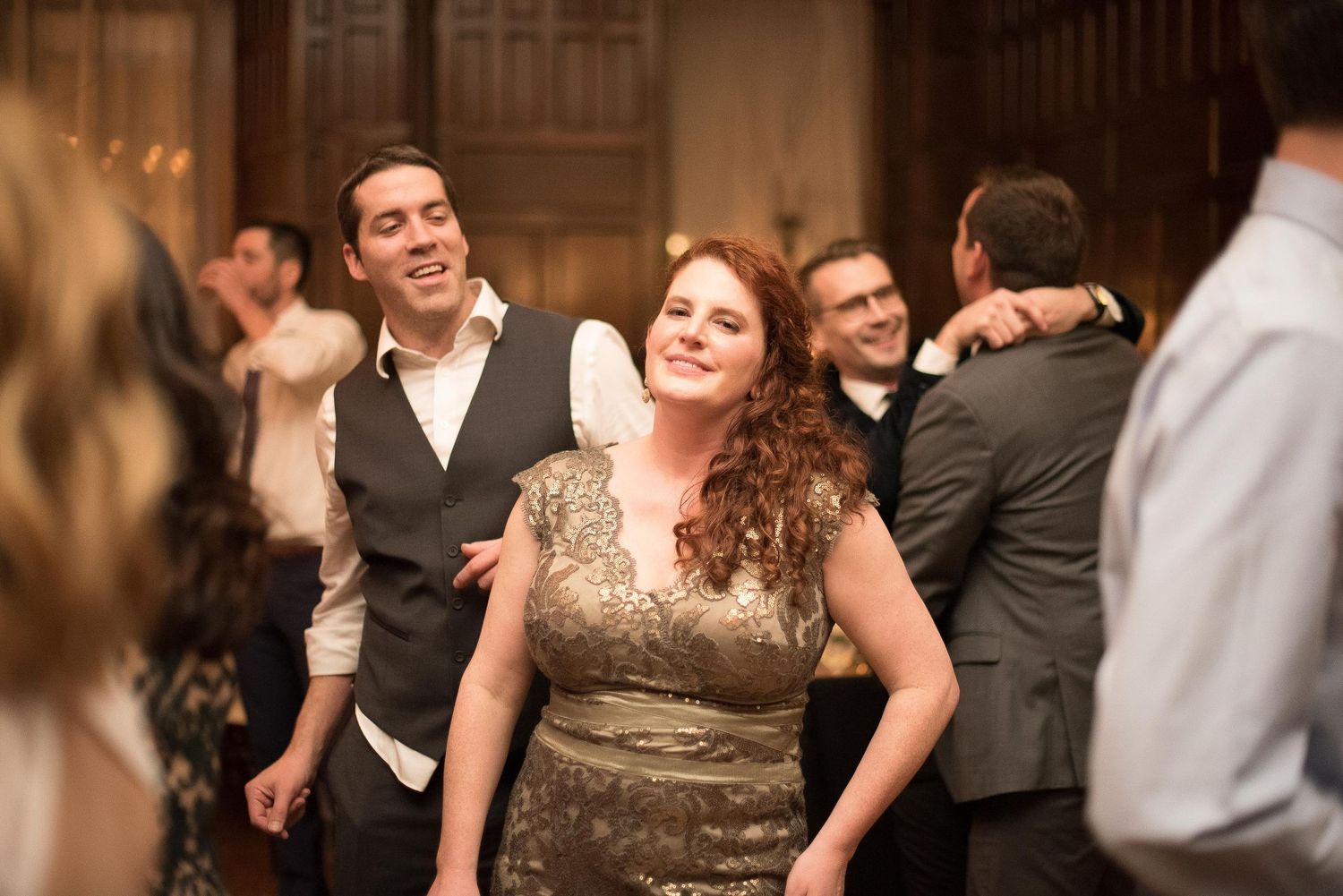 A woman in a gold dress laughs joyfully while dancing at an elegant wedding reception with guests in formal attire.