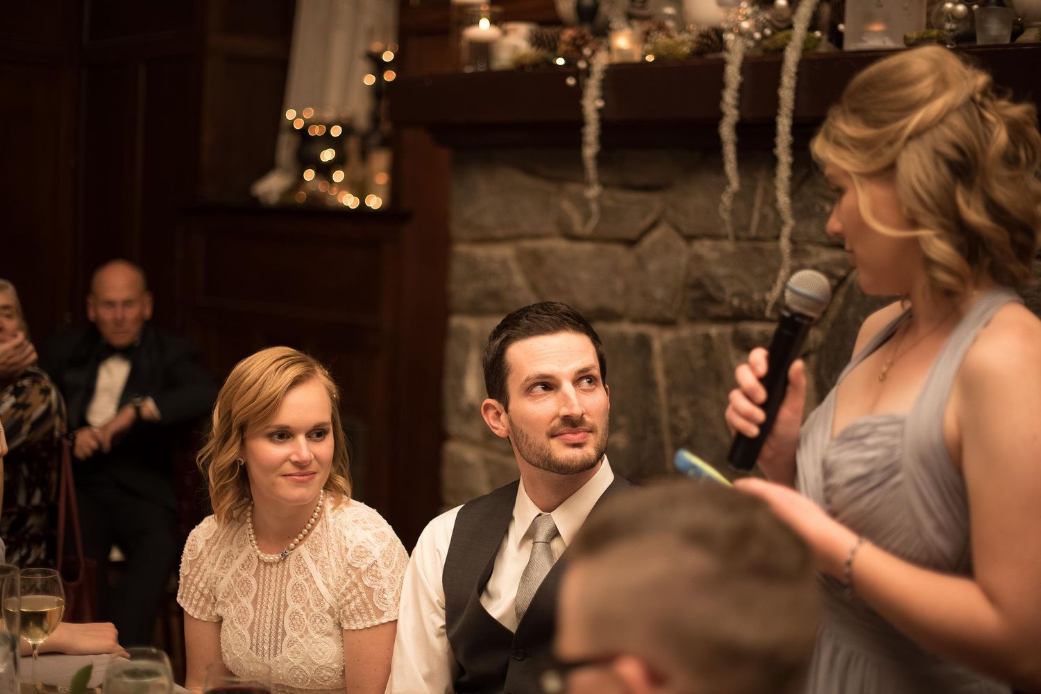 Bridesmaid giving a speech at a wedding reception while the bride and groom listen and smile.