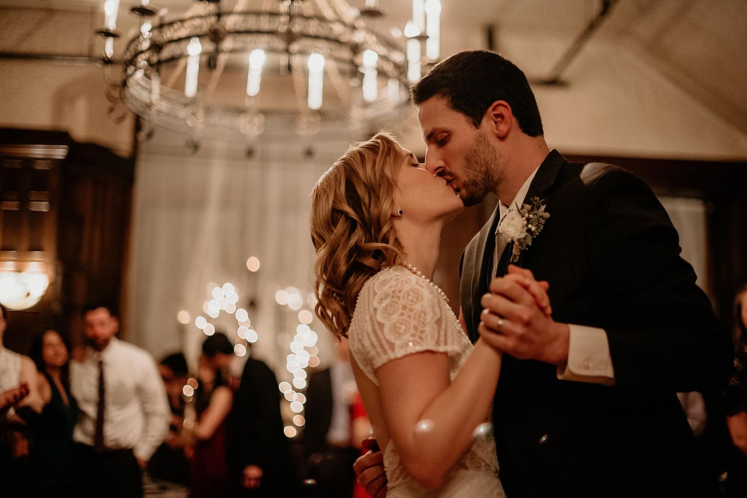 Bride and groom share a first dance kiss under a chandelier at their elegant wedding reception.