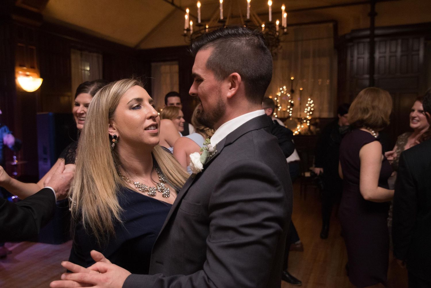 Couple dancing closely at an elegant wedding reception in a warmly lit ballroom with guests in background.